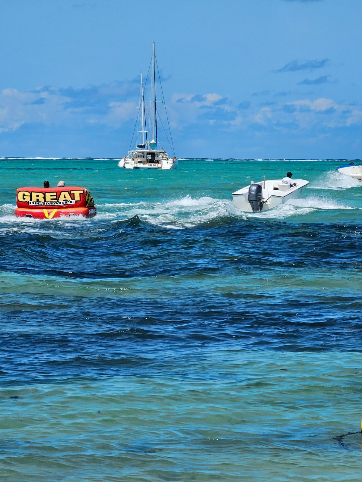 Towable tube and powerboats on turquoise sea near a catamaran